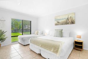 a white bedroom with two beds and a window at Palm Cove House in Trivia in Palm Cove