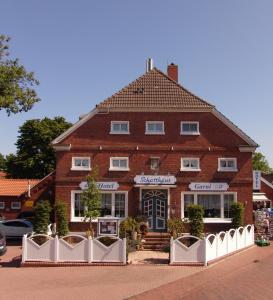 un edificio de ladrillo con una valla blanca delante de él en Hotel Schatthaus en Greetsiel