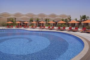 voco - Riyadh, an IHG Hotel في الرياض: مسبح كبير مع كراسي ومظلات في المنتجع
