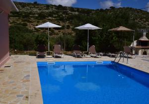 a blue swimming pool with chairs and umbrellas at Moulinos Cottages Kefalonia in Kardhakáta