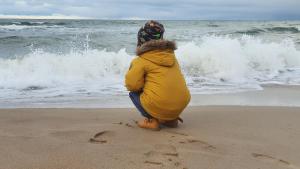 a child sitting on the beach looking at the ocean at Apartament Marzanna w Willi na Klifie in Rewal