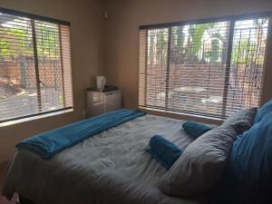 a bed with blue pillows in a room with two windows at Ithiliens Grace Guesthouse in Pretoria +4 photos
