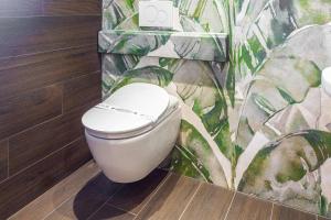 a white toilet in a bathroom with a tropical wallpaper at Costa Rica Bibione SPA in Bibione