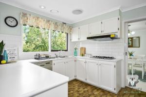 una cucina bianca con mobili bianchi e una finestra di KozyGuru Glen Waverley Family Home & Backyard a Glen Waverley Altre 4 foto
