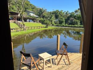 two chairs and a table on a deck with a lake at Pousada Nosso Bosque in Porto Belo