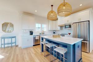 a kitchen with white cabinets and a blue island with stools at Beach Hunters in Holden Beach