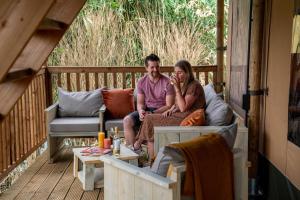 Ein Mann und eine Frau sitzen auf einer Couch auf einer Veranda in der Unterkunft Glamping Rhederlaagse Meren in Lathum