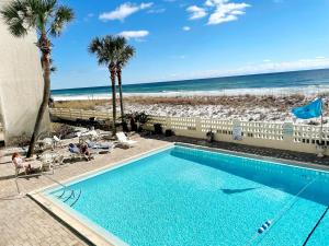 a swimming pool next to a beach with palm trees at Aqua Villa Condo 204 Beachfront in Fort Walton Beach