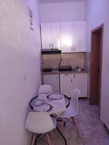 a small kitchen with a table and white chairs at AK apartman in Sutomore