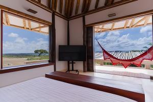 a bedroom with a bed and a tv and two windows at Casa Morro da Luz Bahia in Ilha do Tatu