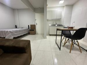 a room with a bed and a table and a kitchen at Studio no coracao do Kobrasol in São José
