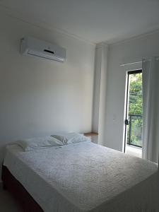 a white bedroom with a bed and a window at Casa geminada 2 no Mariscal in Bombinhas