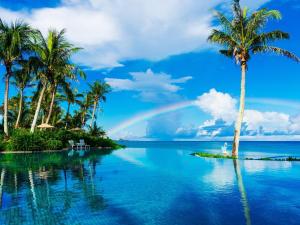 a rainbow over a pool with palm trees and the ocean at HOTEL MOON BEACH MUSEUM RESORT in Onna
