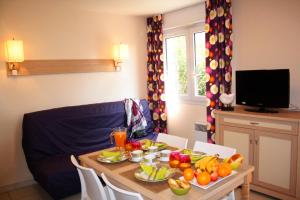 a table with fruits and vegetables on it with a television at Lagrange Grand Bleu Vacances – Résidence Les Pierres de Jade in Saint-Cyprien