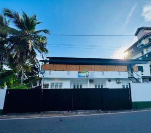 a white building with a fence and a palm tree at Win Min Apartments - Unit D in Homagama