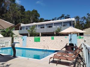 a swimming pool with chairs and umbrellas next to a building at Canto Verde Aptos II in Caraguatatuba