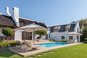 a house with a swimming pool with chairs and an umbrella at Die Rietdak - Reetdachhaus mit vier Schlafzimmern in Cape Town