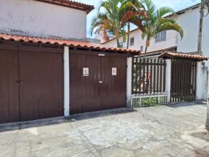a brown garage with a gate and palm trees at Casa da Prainha - a 3min da areia - aproveite até o pôr do sol! in Arraial do Cabo