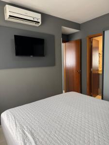 une chambre avec un lit blanc et une télévision à écran plat dans l'établissement Flat Veredas 305 com ar condicionado sala - 300 metros do Hot Park, à Rio Quente