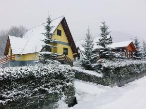 a yellow house with snow on the roof and trees at Kuća za odmor VITICA s vanjskim kaminom in Kupres +8 photos