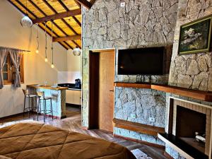 a bedroom with a stone wall with a flat screen tv at Chalés Recanto Vista do Valle in Monte Verde
