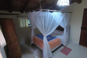 a bedroom with a canopy bed with curtains and a light at Casa Macacos in Porto Seguro