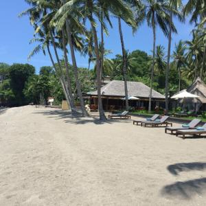 a beach with chaise lounges and palm trees at The Chandi Boutique Resort & Spa in Senggigi