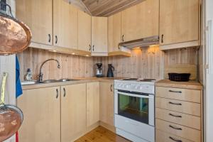 a kitchen with wooden cabinets and a white stove top oven at Koselig hytte i Lofoten, sjø, fjellutsikt, parkering in Laukvik +18 photos