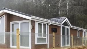a small wooden house with white windows at Woodland Lodge in Plumbland