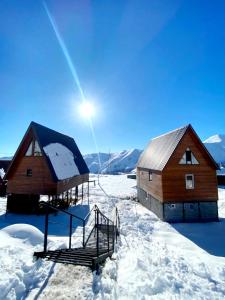 two wooden cabins in the snow with the sun behind them at Chalet Gudauri in Gudauri