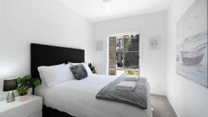 a white bedroom with a large bed and a window at Marine Adventures in Callala Bay