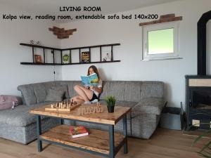 a woman sitting on a couch reading a book while playing chess at RELAX HOUSE Kolpa view Podzemelj in Gradac +57 photos