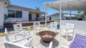 einen Hinterhof mit weißen Stühlen und einer Feuerstelle in der Unterkunft Coastal Palms in Culburra Beach