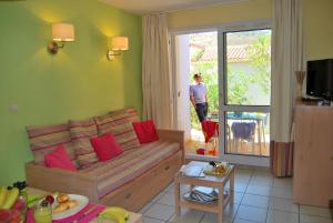 een woonkamer met een bank en een man die uit het raam kijkt bij Lagrange Grand Bleu Vacances – Résidence Le Village des Aloès in Cerbère