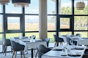 a dining room with tables and chairs and windows at Thalazur Ouistreham - Hôtel & Spa in Ouistreham