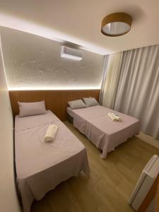 zwei Betten in einem Hotelzimmer mit weißen Laken in der Unterkunft Bangalô Aconchegante - Praia Dulé ES in Guarapari