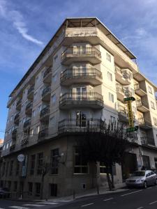 a tall building with balconies and a car parked in front of it at Hotel Derby in Carballino