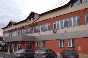 dos autos estacionados frente a un edificio rojo en Motel Maestro, en Deva