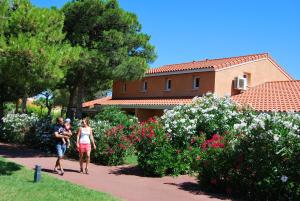 a group of people walking down a path near flowers at Lagrange Grand Bleu Vacances – Résidence Le Mas de Torreilles in Torreilles