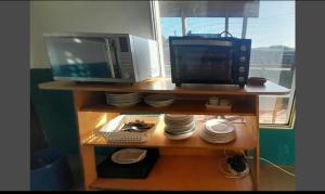 a microwave and a television on a shelf with plates at Balconada Rooms in La Paloma