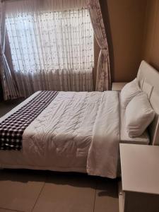 a bed with white sheets and a window with a curtain at Tina's Place in Lilongwe