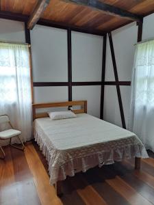 a bedroom with a bed and a chair and windows at Caminhos da Serra do Tabuleiro - Casa Centenária Enxaimel 1915 in São Bonifácio