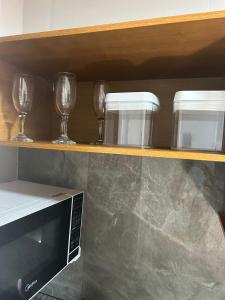 a shelf with wine glasses and a microwave on it at Estúdio Aconchegante no centro de Miguel Pereira in Miguel Pereira