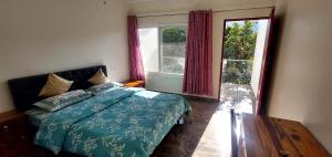 a bedroom with a bed with a blue comforter and two windows at Nileshwar Home Stay in Bāgeshwar +21 photos