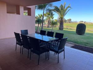 a glass table and chairs on a patio with palm trees at Beautiful 2 Bed Apartment Mar Menor Golf Resort in Los Martínez