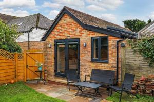 a small brick house with chairs and a table at Cottage in the heart of award-winning English village in Woodchurch