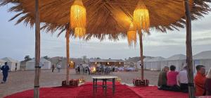 a group of people sitting under a straw umbrella on a beach at Touaregs Camp Erg Lihoudi in Mhamid