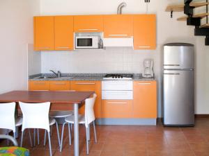 eine Küche mit orangefarbenen Schränken, einem Tisch und einem Kühlschrank in der Unterkunft Holiday Home La Quercia-2 by Interhome in La Fagiana