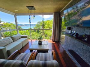 a living room with a couch and a large window at Refúgio da Lagoinha - Centro de Bombinhas in Bombinhas