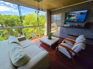 a living room with a white couch and a large window at Refúgio da Lagoinha - Centro de Bombinhas in Bombinhas